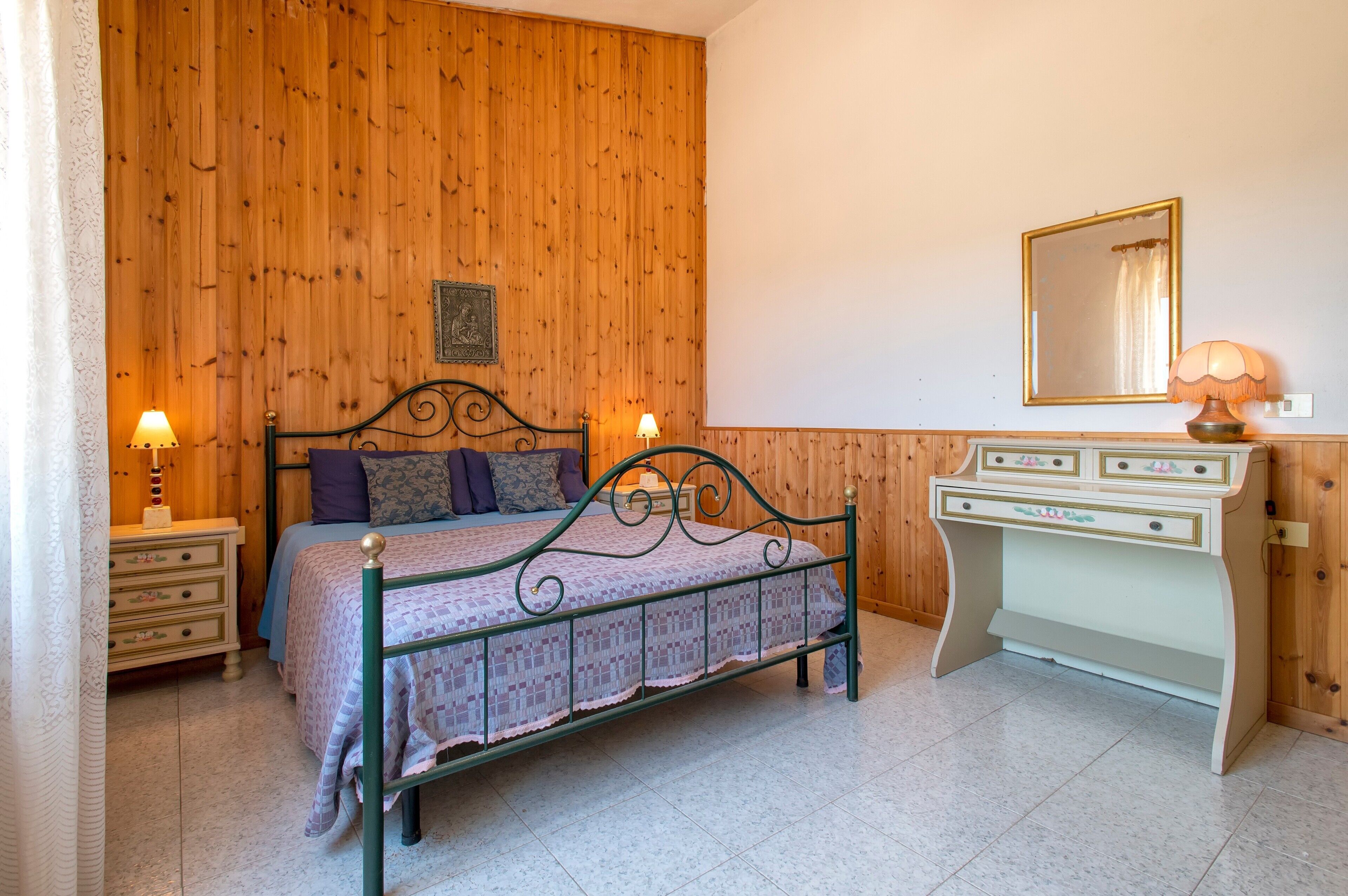 Un dormitorio con cama, dos mesitas de noche con lámparas, cómoda y espejo en la pared.