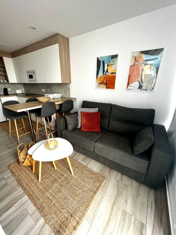 Un espace de vie moderne avec un canapé gris, une petite table ronde et une cuisine en arrière-plan.
