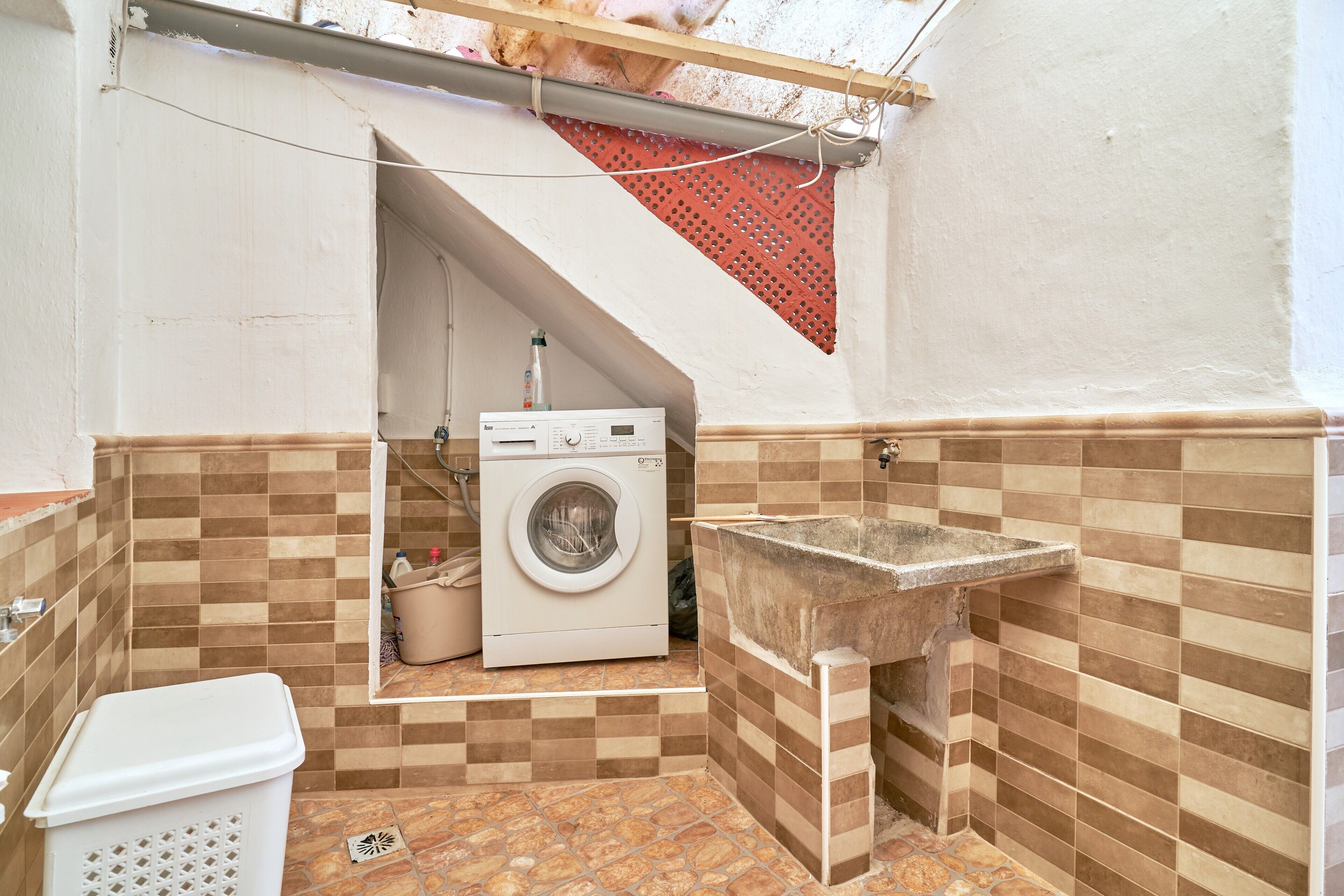 Un bany petit amb rentadora, un lavabo i terra de rajola.