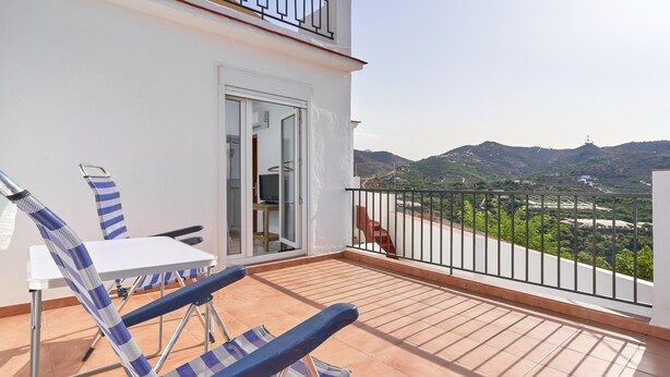 A balcony with a table and chairs, a TV, and a view of green hills. - Holiday Home 'Rafalita' with Sea View, Wi-Fi and Air Conditioning (Torrox)
