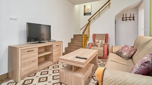 A living room with a TV, wooden furniture, a sofa, a staircase, and a wall-mounted coat rack. - Holiday Home 'Rafalita' with Sea View, Wi-Fi and Air Conditioning (Torrox)