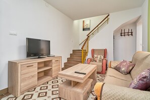 Un salon équipé d’un téléviseur, de meubles en bois, d’un canapé, d’un escalier et d’un porte-manteau fixé au mur.