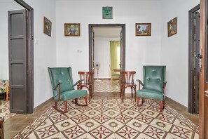 A hallway with patterned floor tiles, two green upholstered chairs, a wooden table, and a door on the left. - Holiday Home 'Rafalita' with Sea View, Wi-Fi and Air Conditioning (Torrox)