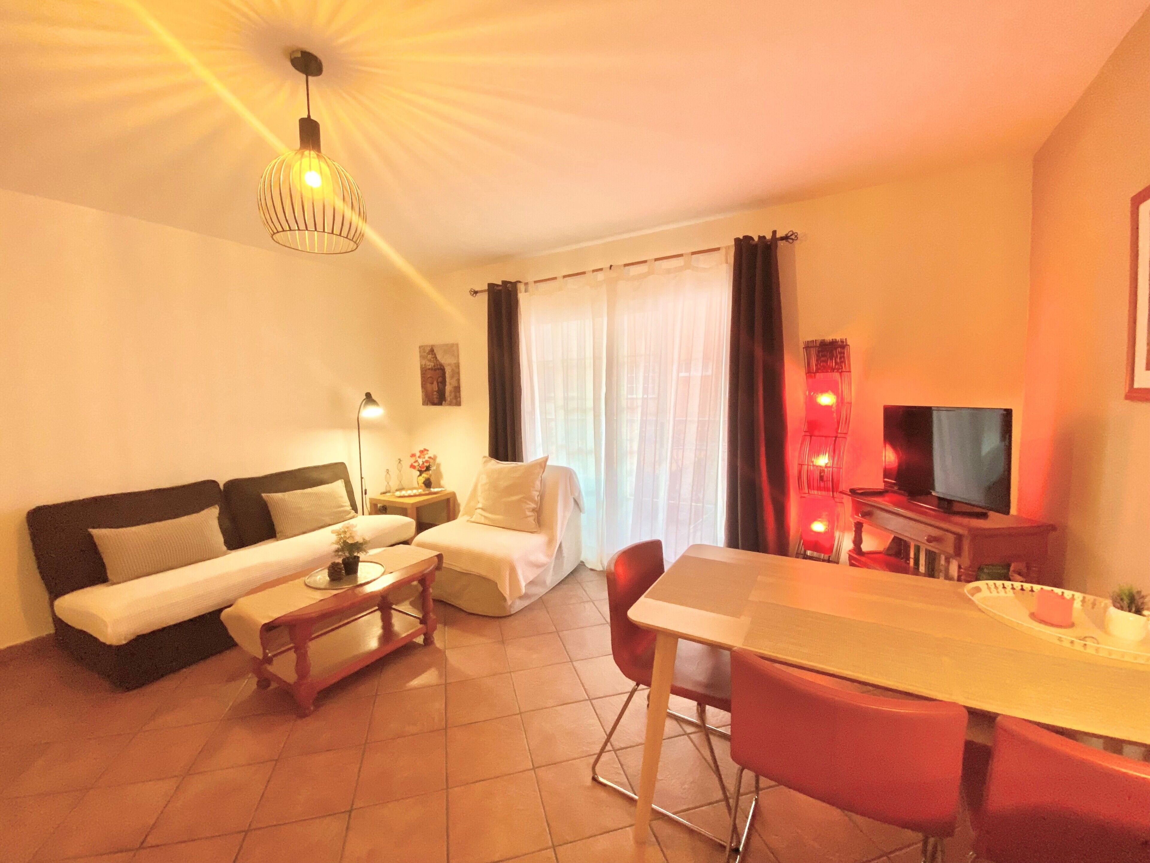 A furnished living room with a sofa, a small table, a chair, a TV, and a lamp.