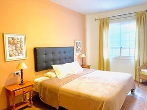 Una camera d'albergo con un letto, due comodini con lampade, una finestra con tende e due quadri appesi al muro.