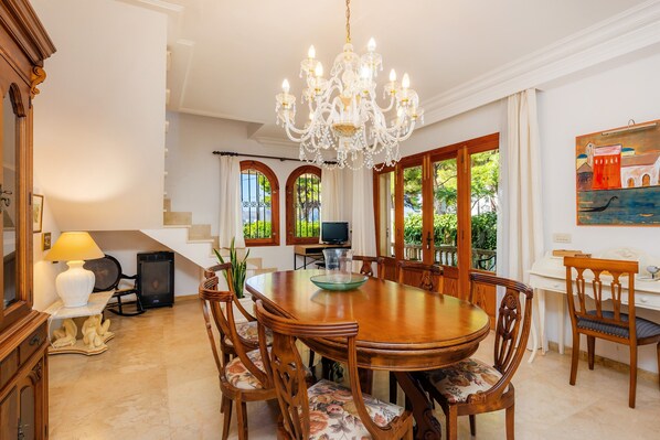 A dining room with a chandelier, wooden table, chairs, and a television.