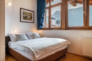 Un dormitorio con cama, ventana con vista a montañas, un cuadro enmarcado en la pared y un radiador.