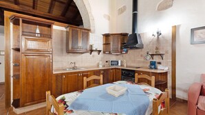 Una cocina con armarios de madera, microondas, cafetera y una mesa de comedor con mantel a cuadros.