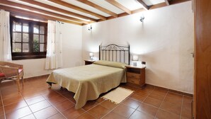 Un dormitorio con cama, mesitas de noche, una ventana con cortinas y techo de madera.