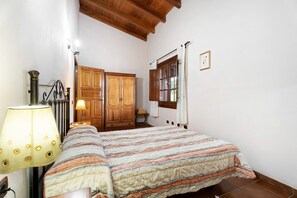 Une chambre à coucher comprenant un lit, une armoire en bois, une fenêtre avec des rideaux, une lampe et un luminaire fixé au mur.