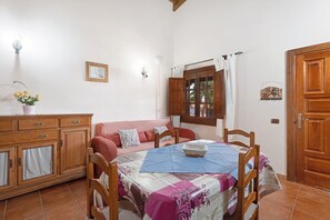 Une pièce comprenant un meuble en bois, un canapé, une table recouverte d’une nappe à carreaux et une fenêtre avec des rideaux.