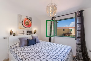 Un dormitorio con cama, ventana con marco verde, lámpara colgante y una obra de arte en la pared.