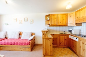 A compact room with a bed, wooden cabinets, a microwave, and a sink.