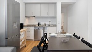 Una cocina moderna con armarios blancos, un refrigerador de acero inoxidable, un lavavajillas y un comedor con una mesa dispuesta para dos.