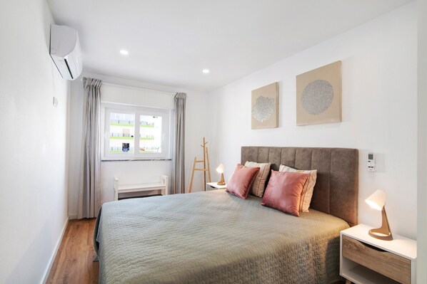 A bedroom with a bed, bedside tables, a window, and artwork on the wall.
