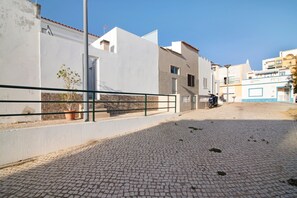 A cobblestone street with buildings, a metal fence, and a clear sky.