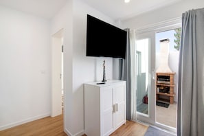 Une pièce avec un meuble blanc, un téléviseur fixé au mur et une porte-fenêtre coulissante donnant sur un espace extérieur doté d’une cheminée en briques.