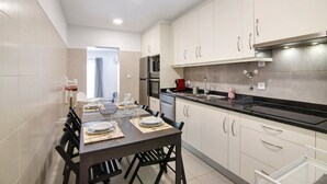 Een moderne keuken met witte kastjes, een zwart aanrecht en een eethoek met een tafel voor vier personen.
