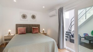 Een slaapkamer met een bed, nachtkastjes, wanddecoratie, een airconditioning en een trap, met uitzicht op buiten.