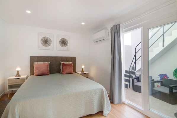 Une chambre à coucher comprenant un lit, des tables de chevet, des œuvres d’art mural, un appareil de climatisation, un escalier et une vue sur l’extérieur.