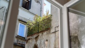 A narrow alleyway with a building featuring a window with a blue shutter, a small door, and a wall with a metal fence and some greenery. - Vico Sedil Capuano 21 - Appartamento 1 (Naples)