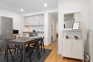 A modern kitchen with white cabinets, a dining table with chairs, and a small refrigerator.