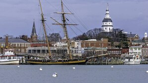 Un navire historique était amarré dans un port, avec une église imposante et un bâtiment à dôme blanc en arrière-plan.