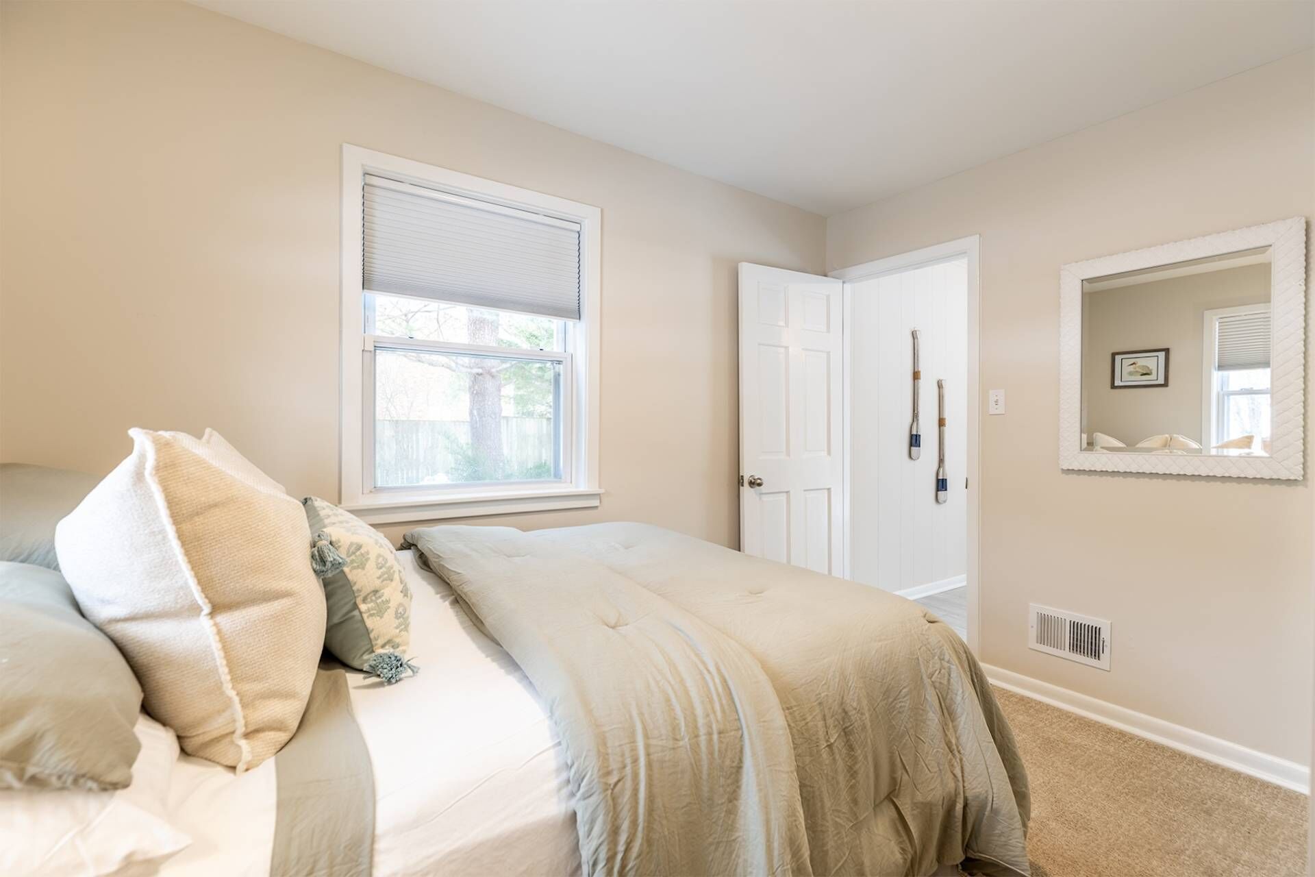 A bedroom with a bed, a window with blinds, a door, and a mirror on the wall.