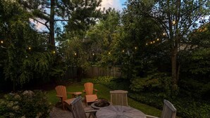 Une terrasse dotée de chaises en bois et d’une table ronde, entourée d’une végétation luxuriante et d’arbres.