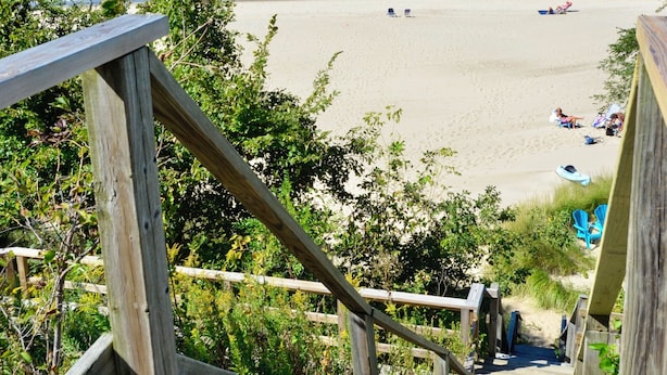 A wooden staircase leading to a beach with clear blue water and a sandy shore.
