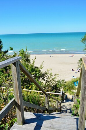 Una escalera de madera que conduce a una playa con agua azul cristalina y una orilla arenosa.