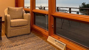 A cozy room with a large window overlooking a wooden deck and a body of water.