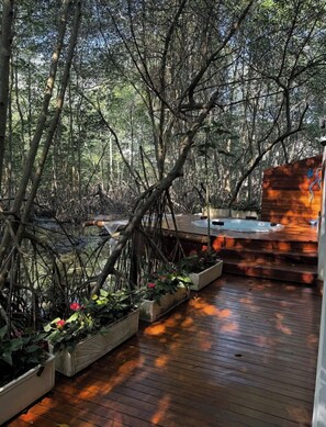 Une terrasse en bois agrémentée de jardinières et d’un jacuzzi, le tout entouré d’arbres denses.