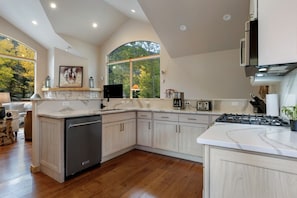 Une cuisine moderne équipée d’un lave-vaisselle, d’une cuisinière et de grandes fenêtres donnant sur la verdure.