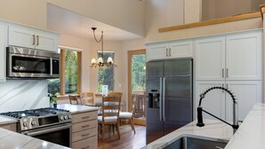 Una cocina moderna con armarios blancos, electrodomésticos de acero inoxidable, una isla central y un comedor con sillas de madera y una araña.