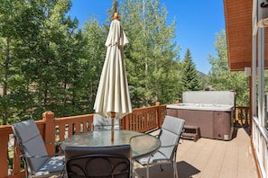 Une terrasse avec une table en verre, des chaises, un parasol et un jacuzzi.