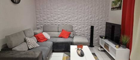 A modern living room with a grey sectional sofa, a white coffee table, and a TV stand.