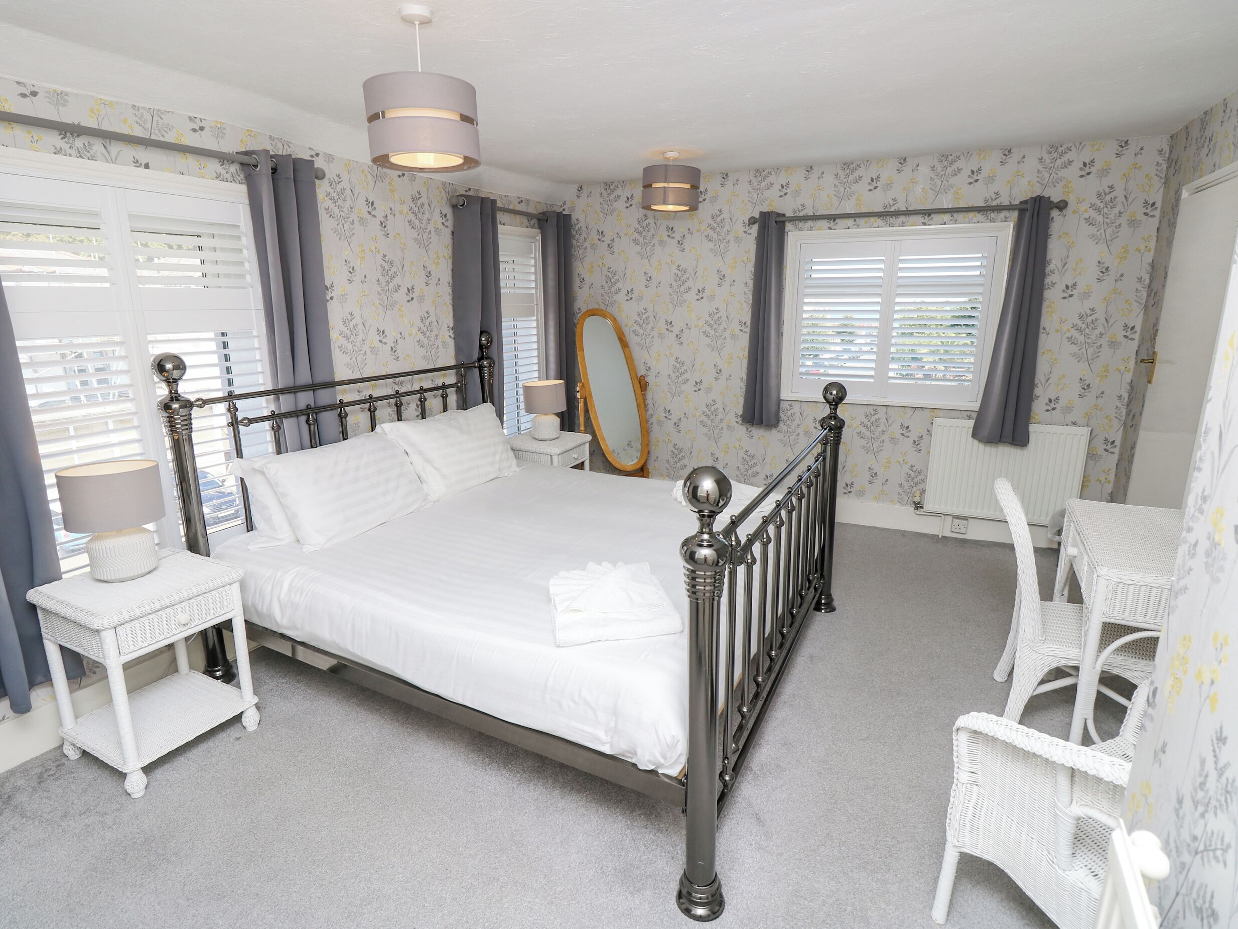 A neatly arranged bedroom with a bed, bedside tables, a mirror, and a chair.