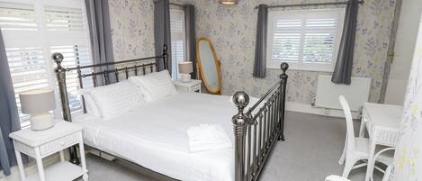 A neatly arranged bedroom with a bed, bedside tables, a mirror, and a chair.