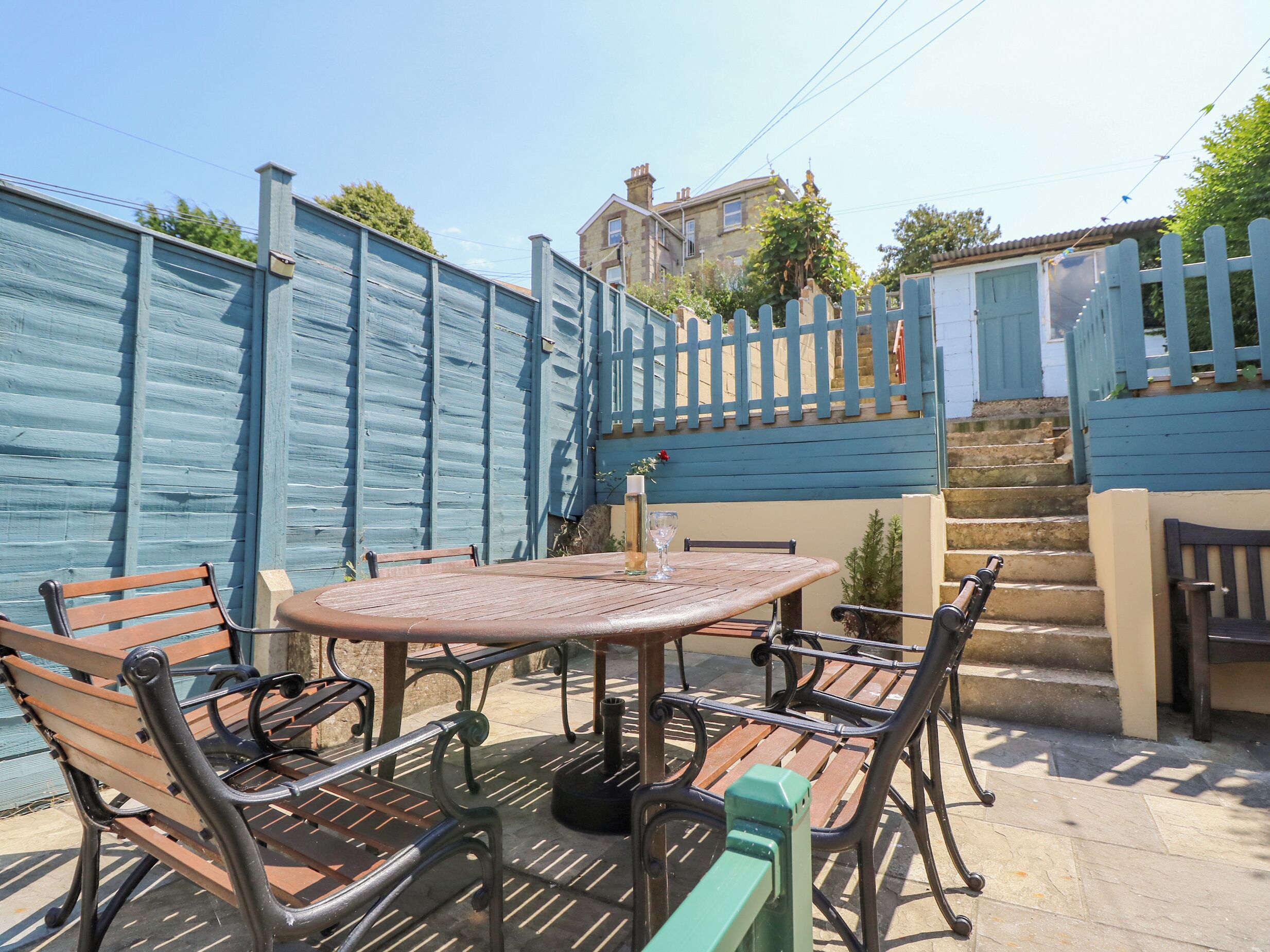 An outdoor patio area with a round metal table and four wooden chairs.