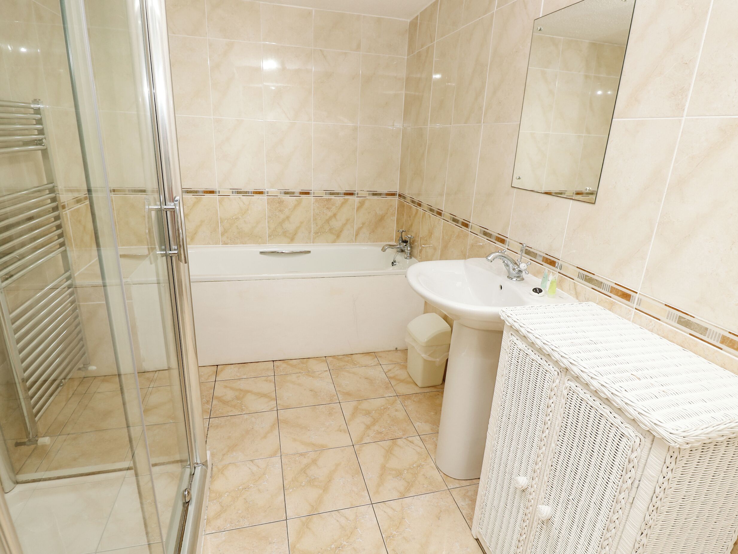 A bathroom with a glass shower enclosure, a bathtub, a sink, and a wicker vanity.