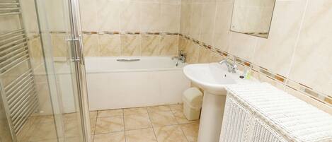 A bathroom with a glass shower enclosure, a bathtub, a sink, and a wicker vanity.