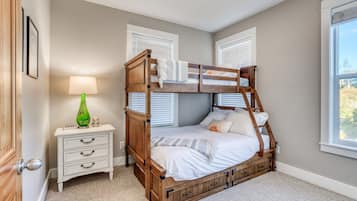 A bunk bed room with a nightstand, lamp, and a window with blinds.