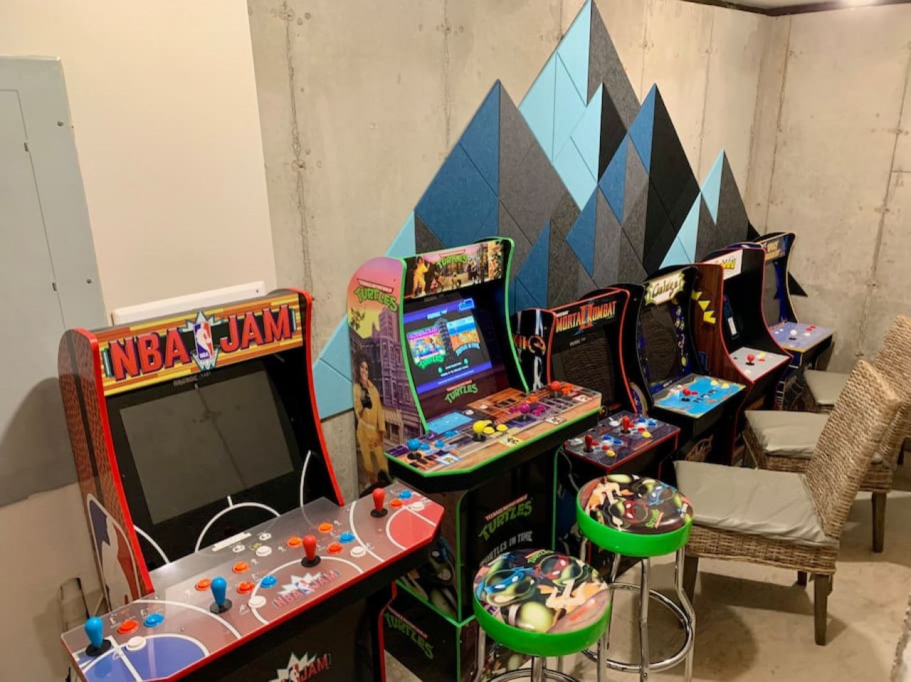 Ein Raum mit Spielautomaten, darunter NBA JAM und Mortal Kombat, sowie ein Korbstuhl.