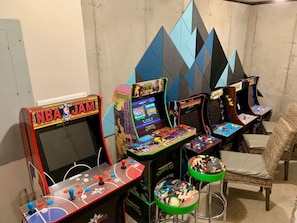Una habitación con máquinas de videojuegos, incluyendo NBA JAM y Mortal Kombat, y una silla de mimbre.