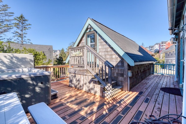 Una terraza de madera con jacuzzi integrado, una escalera y vistas del vecindario circundante.