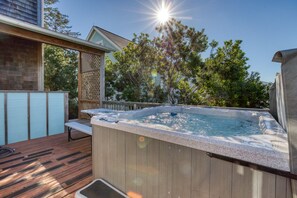 Un jacuzzi en una terraza de madera, con una valla de madera y árboles al fondo.