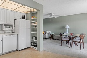 A compact kitchen with a refrigerator, oven, and built-in dishwasher. There is a dining area with a table and chairs.