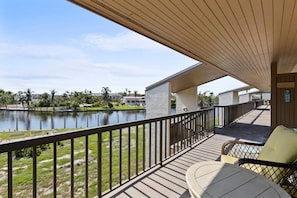 A balcony with a view of a lake, a chair, and a table.