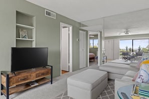 A living room with a flat-screen TV on a wooden stand, a sofa, and a dining area with a table and chairs.
